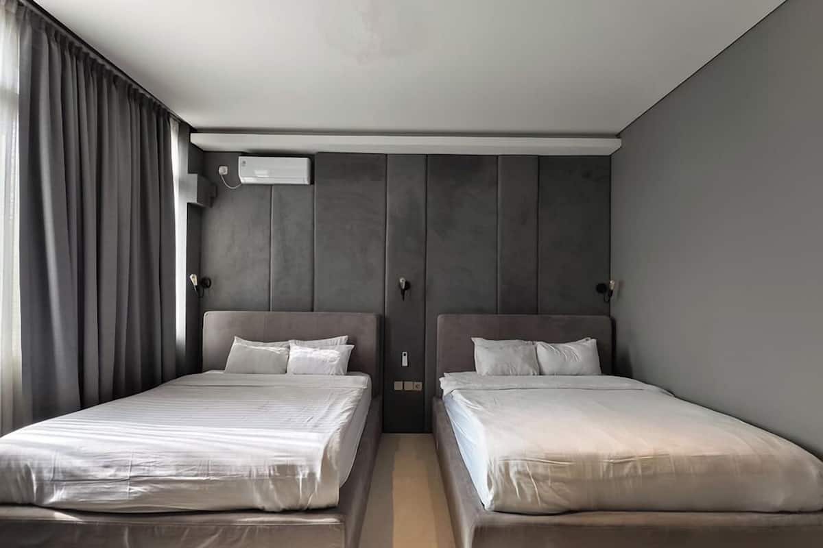 A hotel room with two beds, a large window with curtains, a wall-mounted air conditioning unit, and a neutral color scheme.
