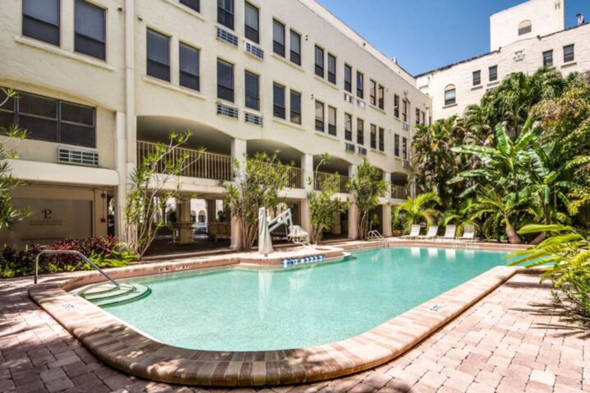 Una piscina con borde de ladrillo, rodeada por un edificio con múltiples balcones y una zona cubierta.