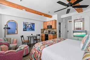 Un dormitorio con cama, ventilador de techo, televisor, kitchenette y mesa de comedor con sillas.