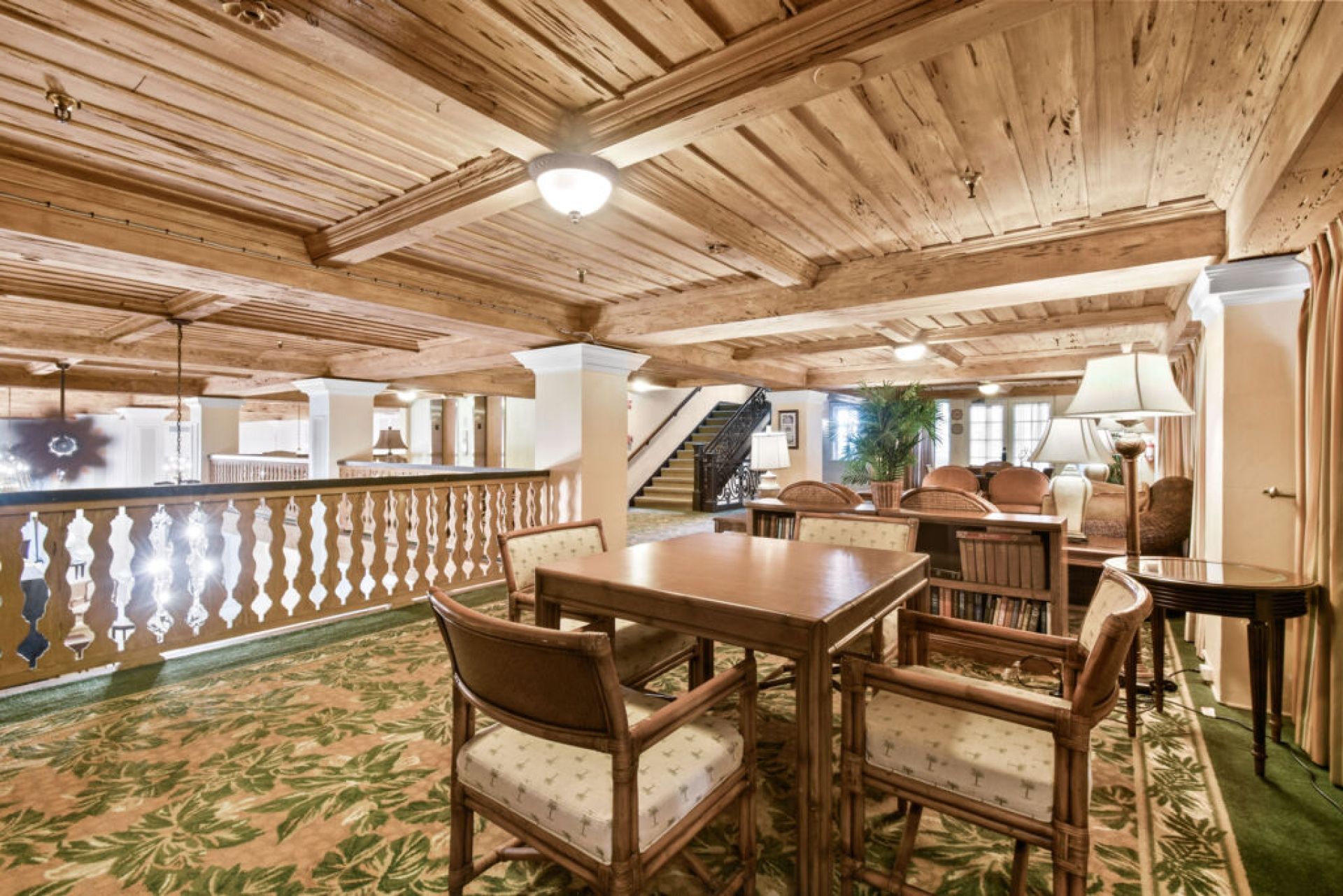 A room with a wooden ceiling, a dining table with chairs, a staircase, and a view of the outside.
