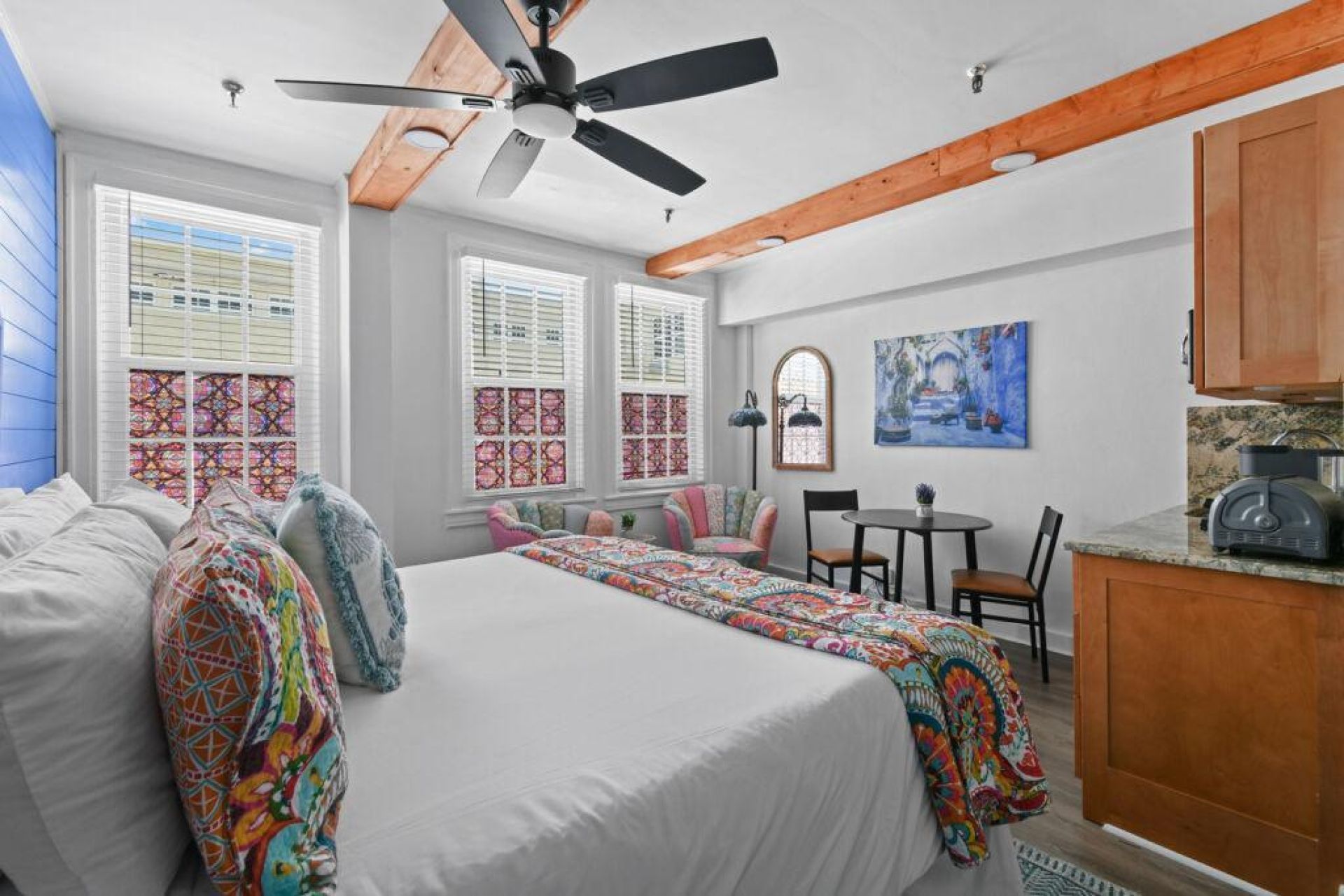 Une chambre avec un grand lit, un ventilateur de plafond et une vue sur la cuisine.