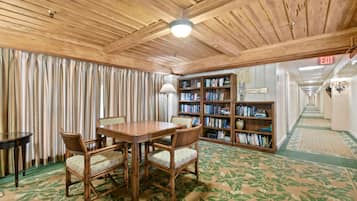 Une pièce avec un plafond en bois, une table entourée de chaises, une bibliothèque et un tapis à motifs.