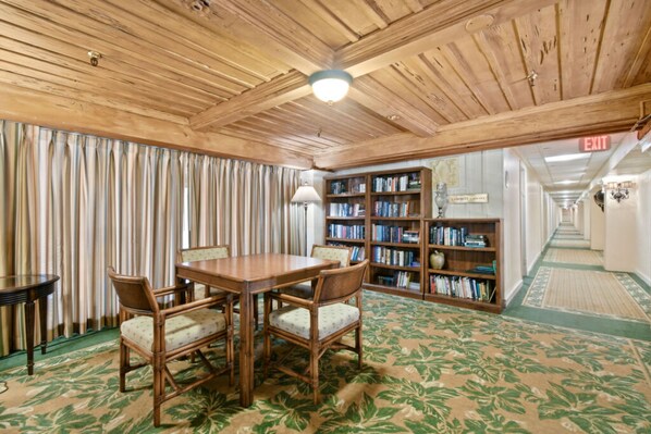 A room with a wooden ceiling, a table with chairs, a bookshelf, and a patterned carpet.