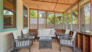 Een overdekt terras met een houten plafond, een bank en vier stoelen.