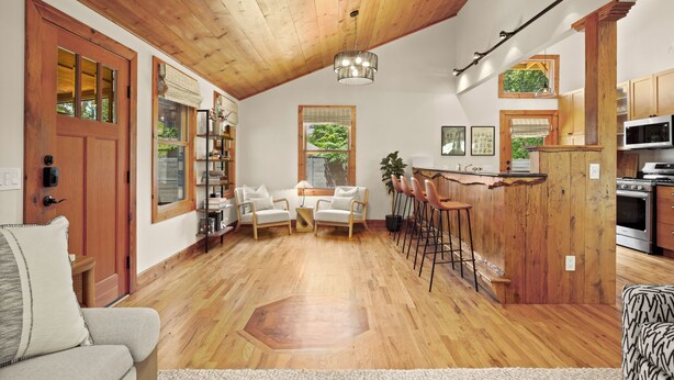 Een ruime woonkamer met houten vloeren, een hoog plafond en een keuken met houten kastjes en moderne apparatuur.