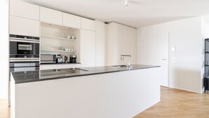A modern kitchen with white cabinetry, a black countertop, and a built-in oven. - Blueground | Alt-Wiedikon, balcony, nr Uetliberg (Zurich)