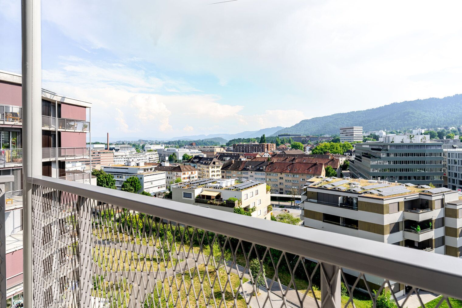 A cityscape with modern buildings, a clear sky, and distant mountains.