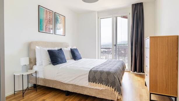 A modern bedroom with a bed, a nightstand, a wardrobe, and a large window with a view. - Blueground | Alt-Wiedikon, balcony, nr Uetliberg (Zurich)
