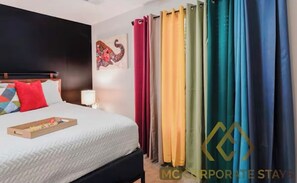 Ein Hotelzimmer mit Bett, Nachttisch, Lampe und einem bunten Vorhang.