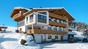A multi-story chalet with wooden balconies, a ski lift in the background, and a snow-covered landscape.