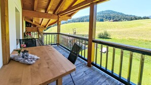 A wooden deck with a table and chairs, overlooking a green field and hills.