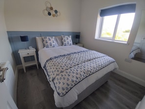 A bedroom with a bed, bedside tables, a wall decoration, a window, and a view of the outdoors. - Apartment - Sleeps 4 - Near Aran Islands - Parking (Galway)