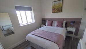 Une chambre à coucher avec un lit, des tables de chevet, une fenêtre, un tableau et un miroir.
