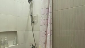 A bathroom with a shower, toilet, and a shelf with toiletries. - Omah Kulon Malioboro (Kasihan)