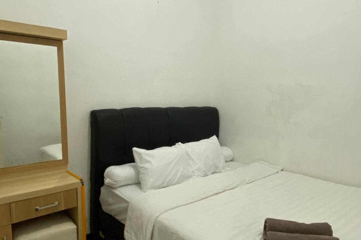 Een kleine, schone kamer met een bed, nachtkastje en spiegel.