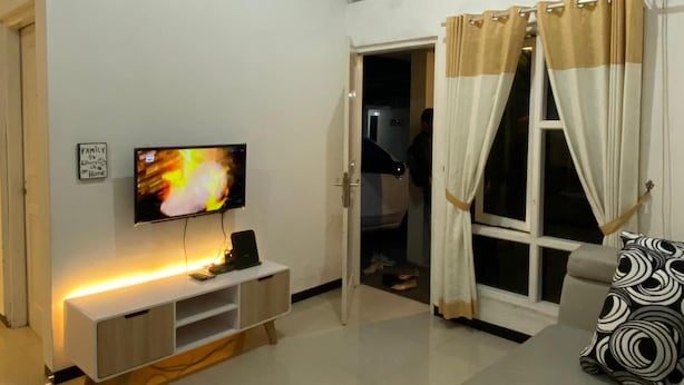 A living room with a flat-screen TV, a sofa, a TV stand, and a window with curtains. - Omah Kulon Malioboro (Kasihan)