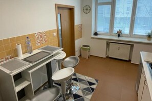 A small kitchen with a sink, two stools, a window with blinds, and a radiator.
