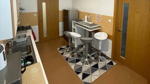 Une cuisine compacte comprenant un évier, deux tabourets, une petite table et un réfrigérateur.