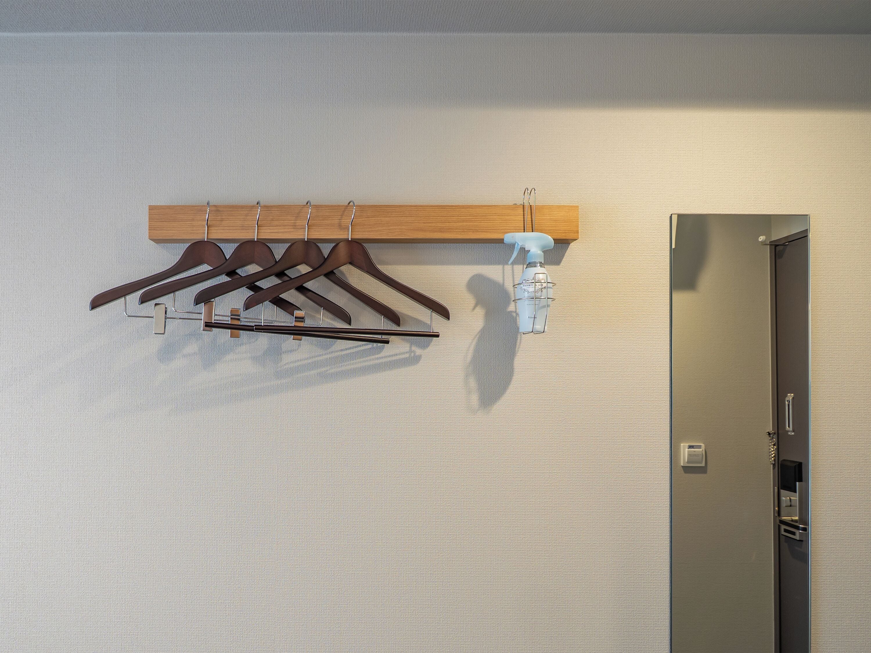 A wall-mounted wooden rack with multiple hangers, a spray bottle, and a door with a handle.