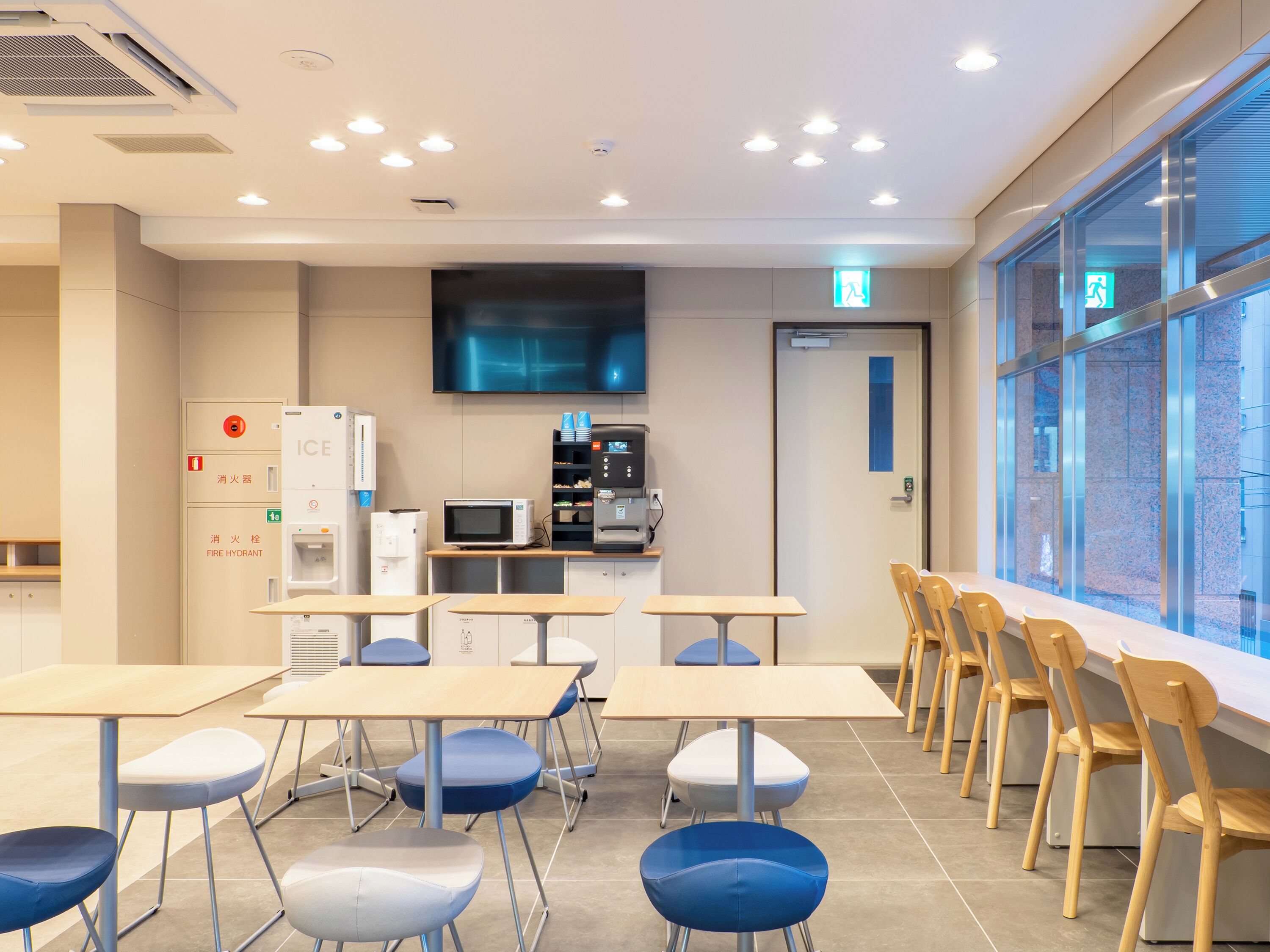 Un aula moderna con mesas, sillas, una pantalla de proyector y una kitchenette.