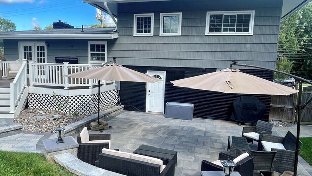 Une terrasse avec des meubles d’extérieur, deux parasols et un foyer en pierre.