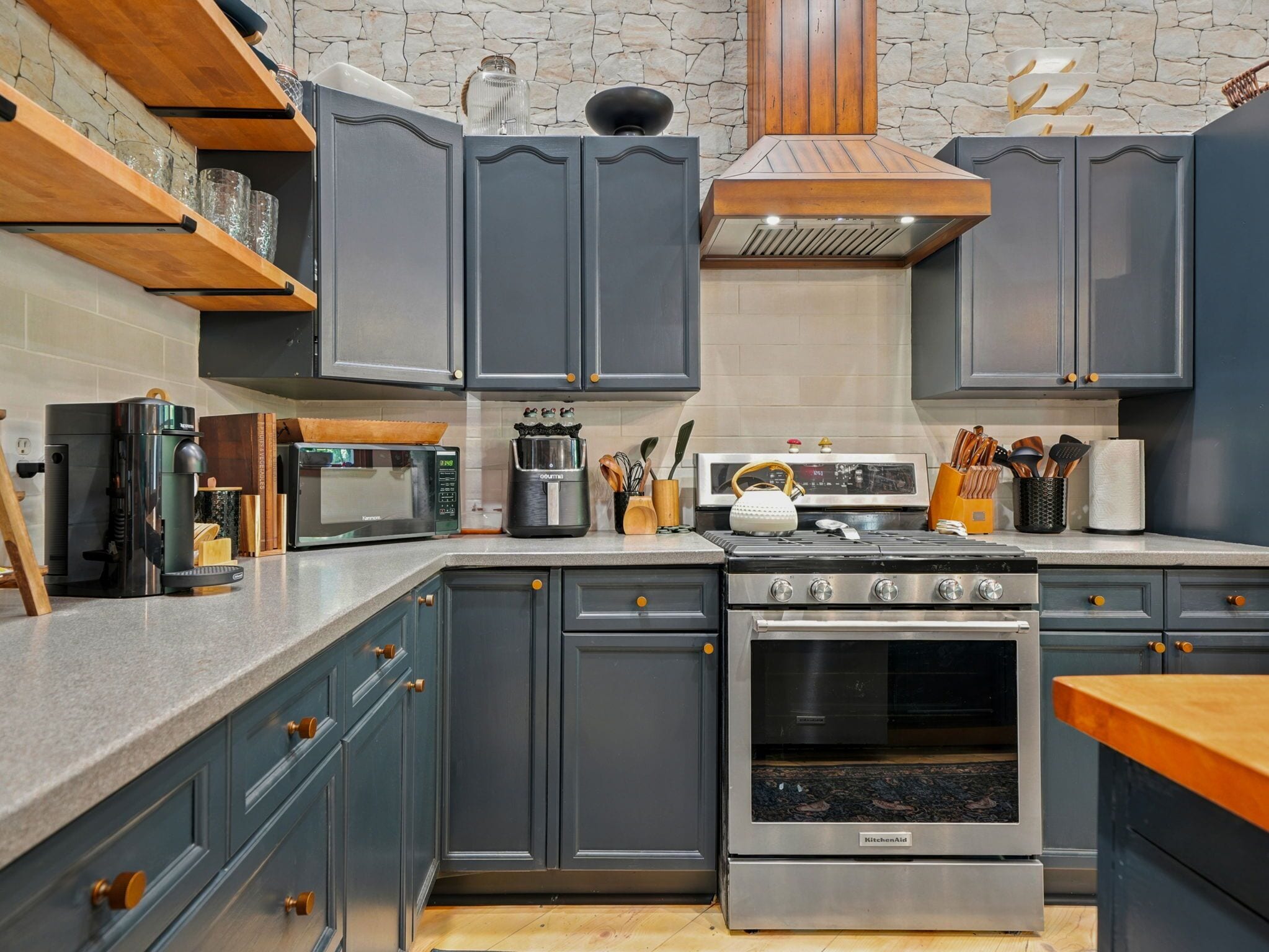 A modern kitchen with grey cabinets, a built-in oven, a microwave, and a coffee maker.