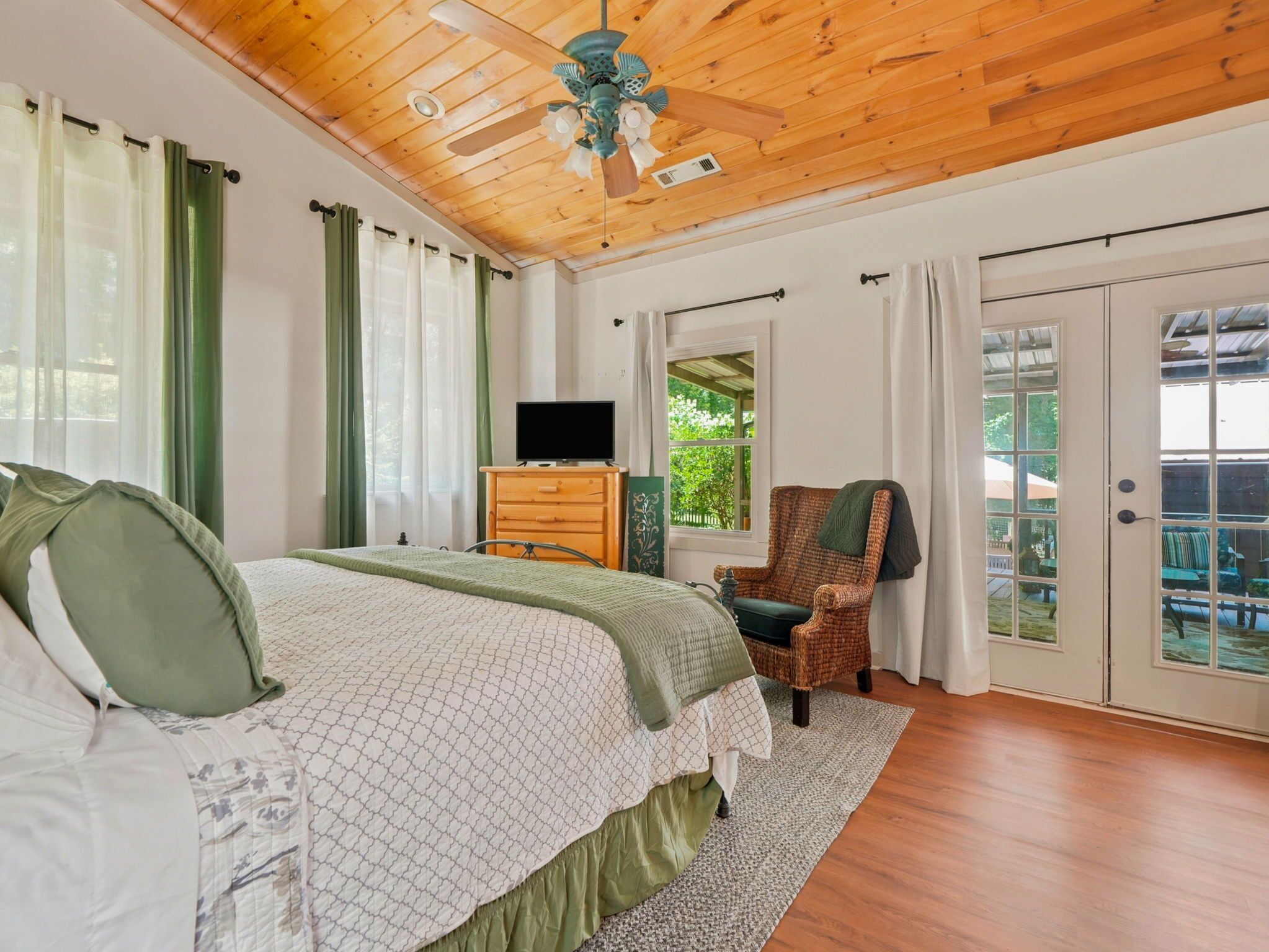 A bedroom with a bed, a dresser, a television, a chair, and a view through a window.
