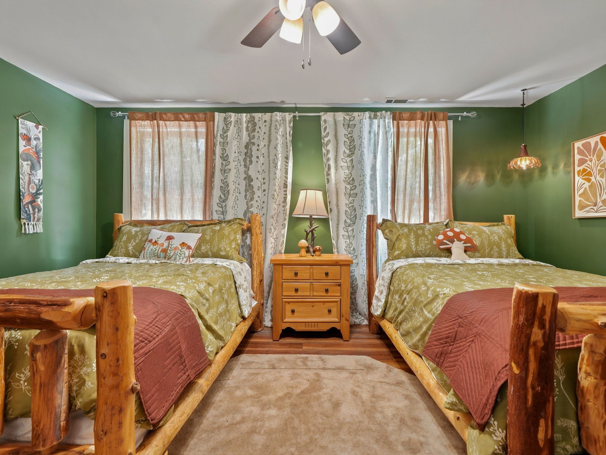 A room with two beds, a wooden nightstand, a lamp, and a ceiling fan.