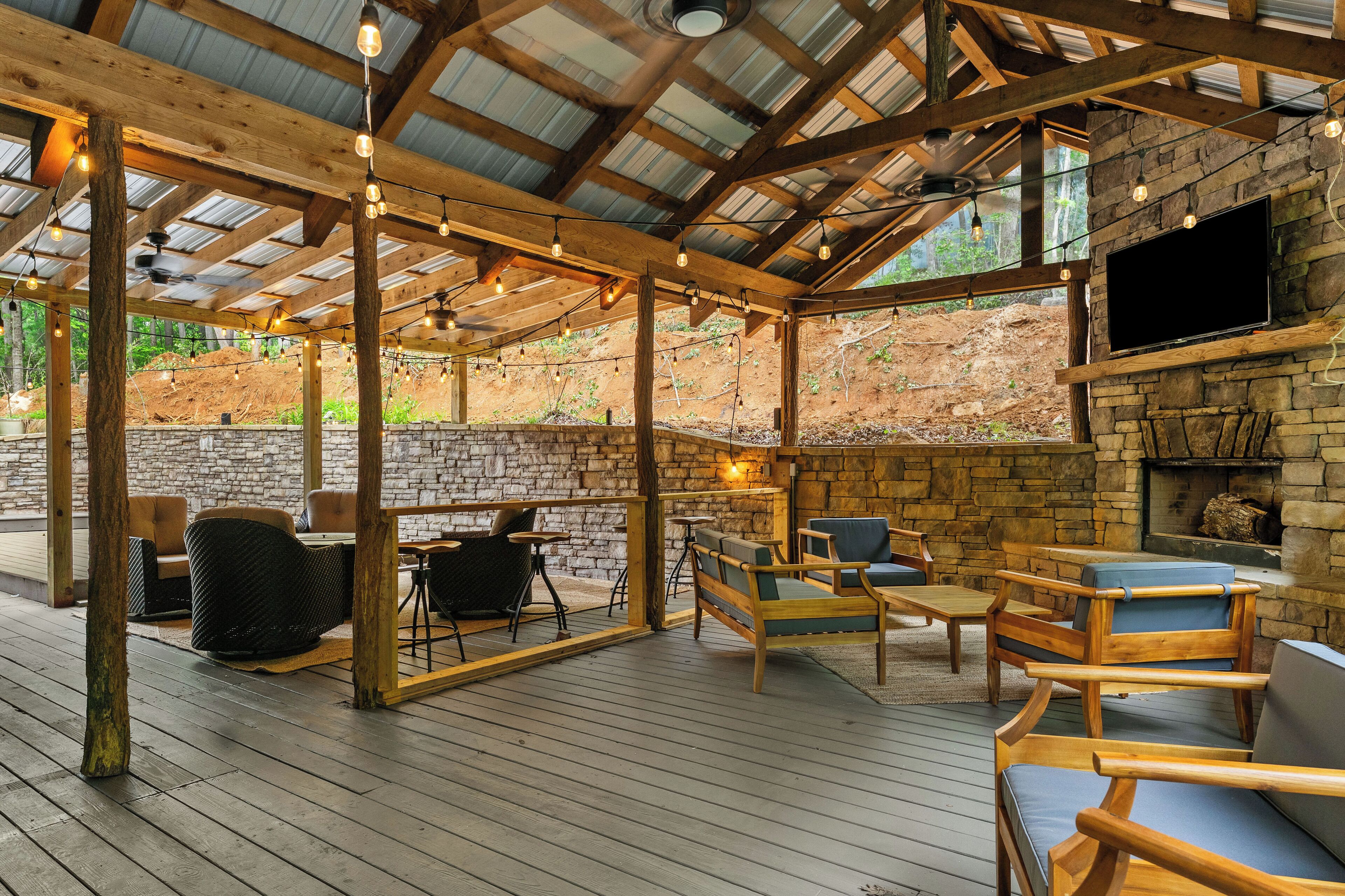 Une terrasse extérieure avec des meubles en bois, des murs en pierre et un téléviseur fixé à un mur en pierre.