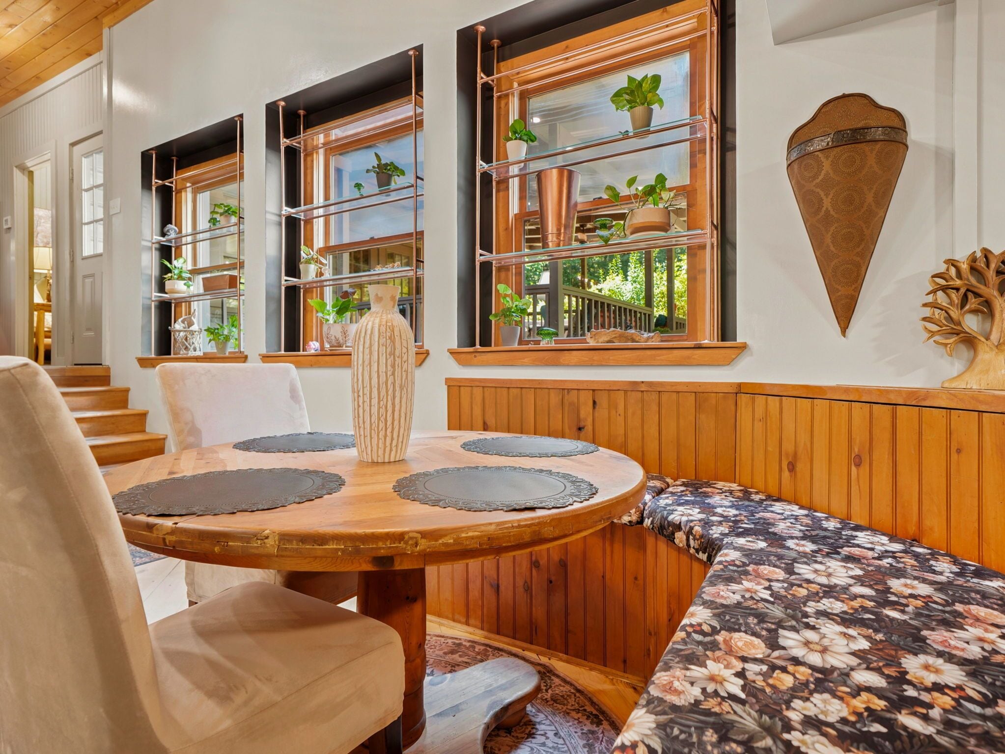 Un comedor con una mesa redonda de madera, un banco acolchado y vistas al exterior.