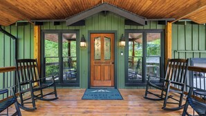 Une véranda en bois avec une porte verte, des fauteuils à bascule et un paillasson.