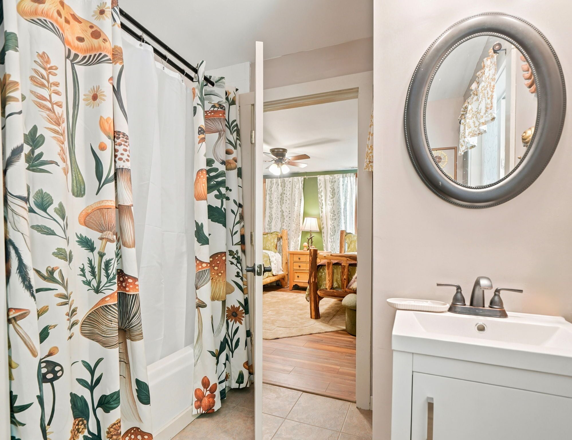 A bathroom with a white sink, a round mirror, and a shower curtain with a nature print.