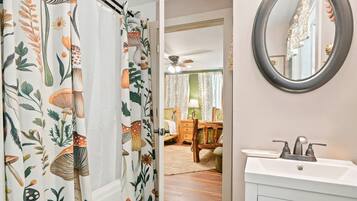 A bathroom with a white sink, a round mirror, and a shower curtain with a nature print.
