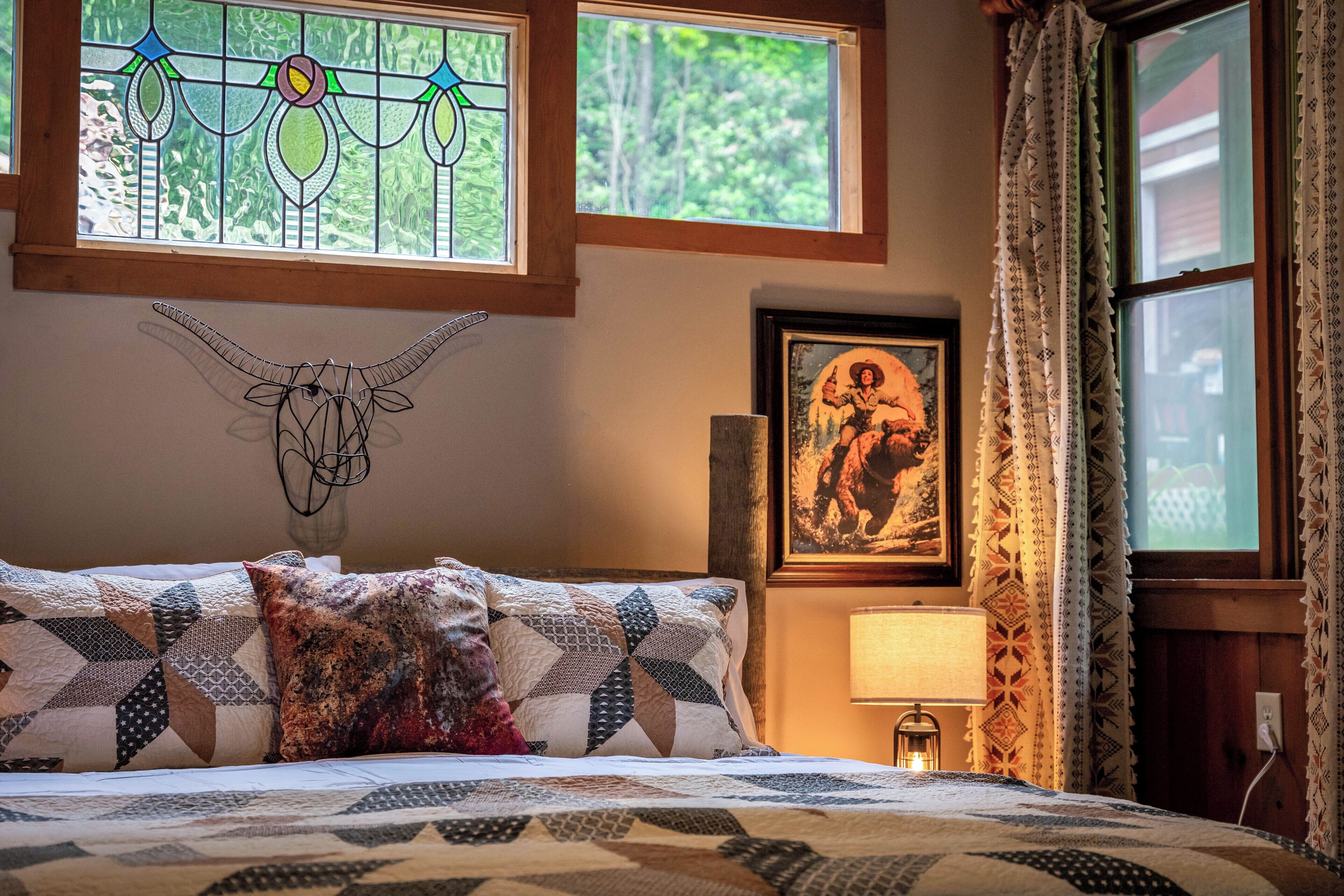 Une chambre à coucher avec un lit, une décoration murale représentant un crâne de vache, un tableau encadré et une fenêtre avec des rideaux.