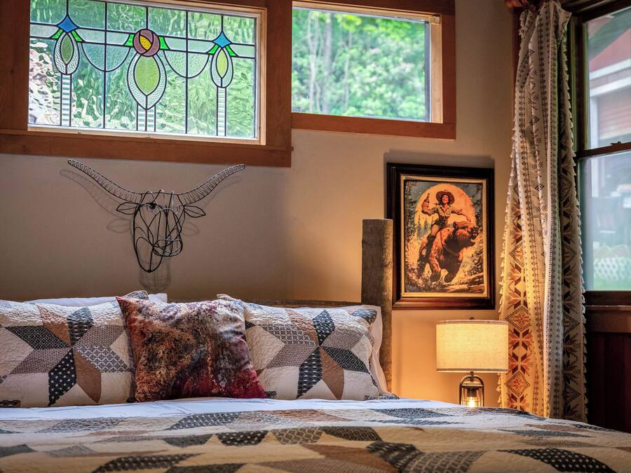 Une chambre à coucher avec un lit, une décoration murale représentant un crâne de vache, un tableau encadré et une fenêtre avec des rideaux.