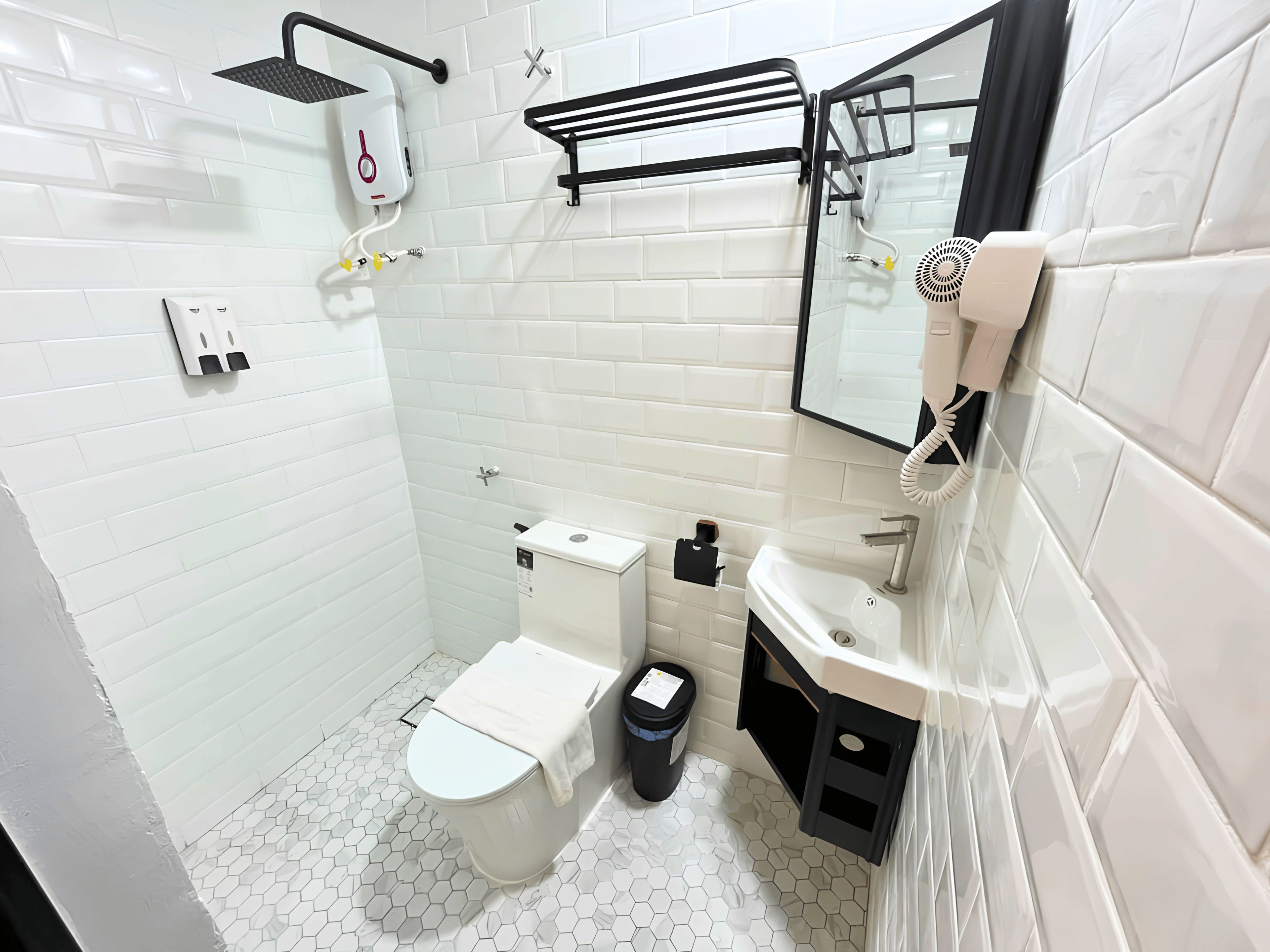 Un baño moderno con azulejos blancos, inodoro, lavabo, espejo, toallero y ducha.