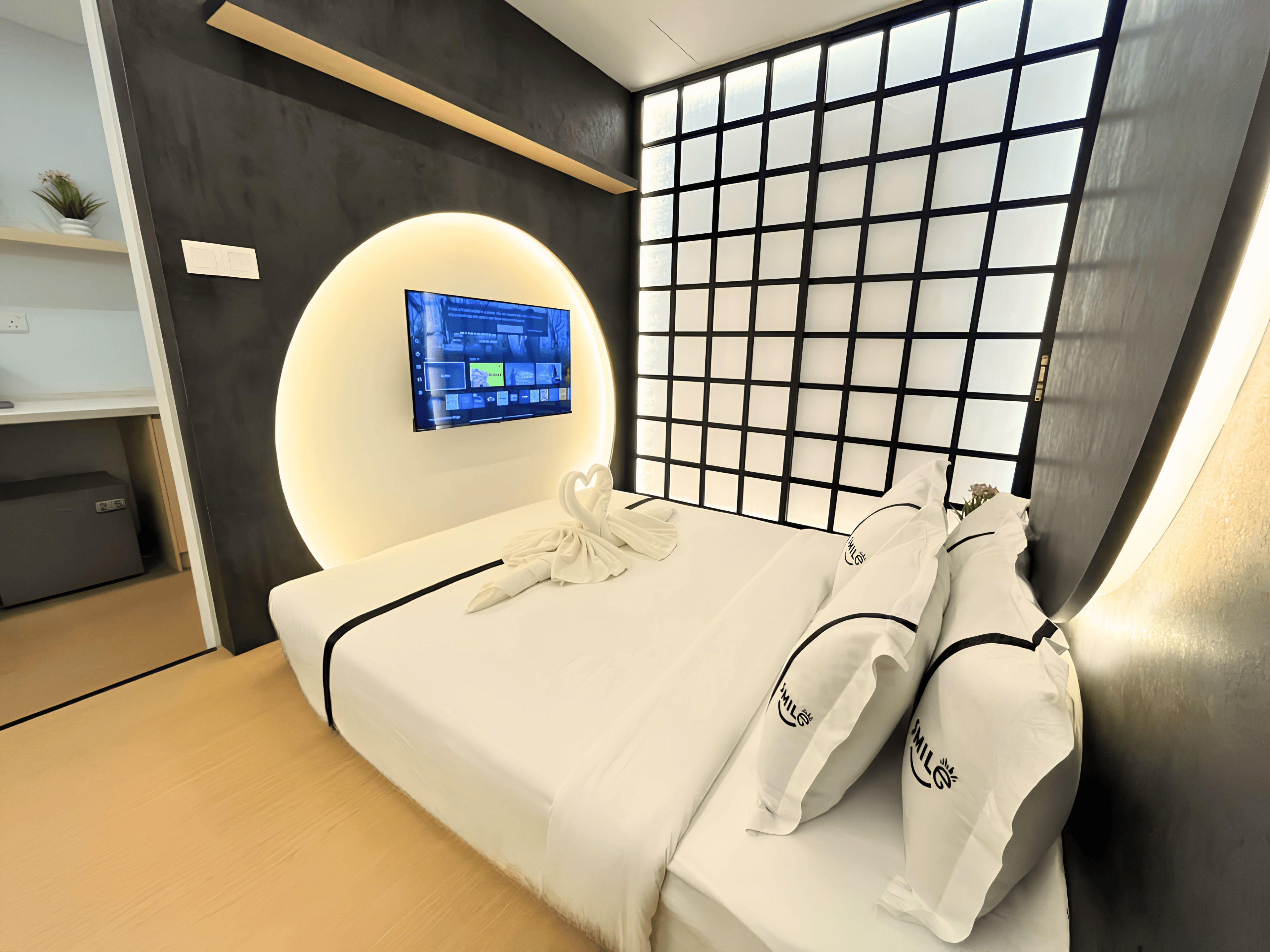Une chambre d’hôtel moderne équipée d’un lit, d’un téléviseur fixé au mur et d’une tête de lit au motif quadrillé original.