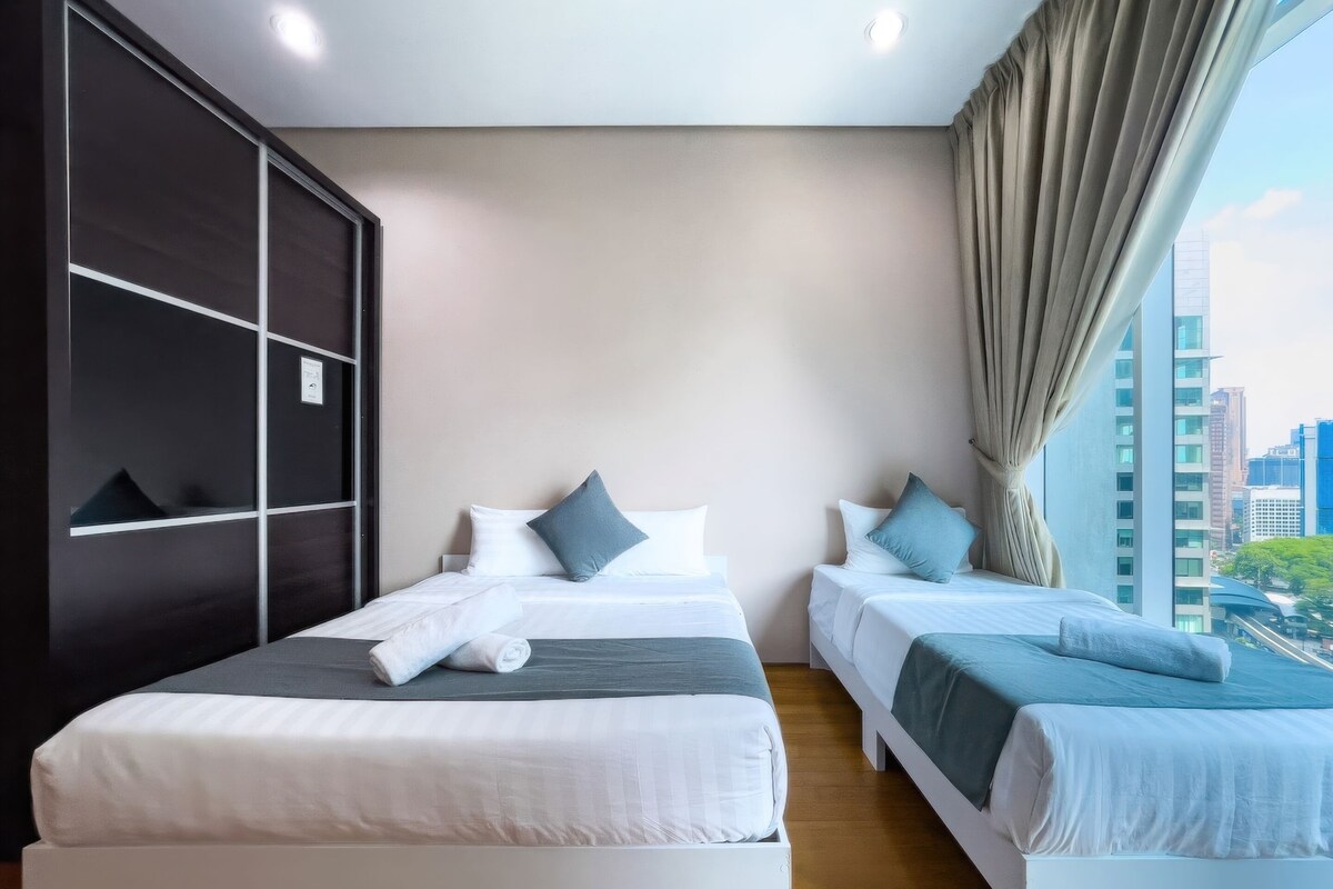 Habitación de hotel con dos camas, un ventanal con cortinas y vista al horizonte de la ciudad.