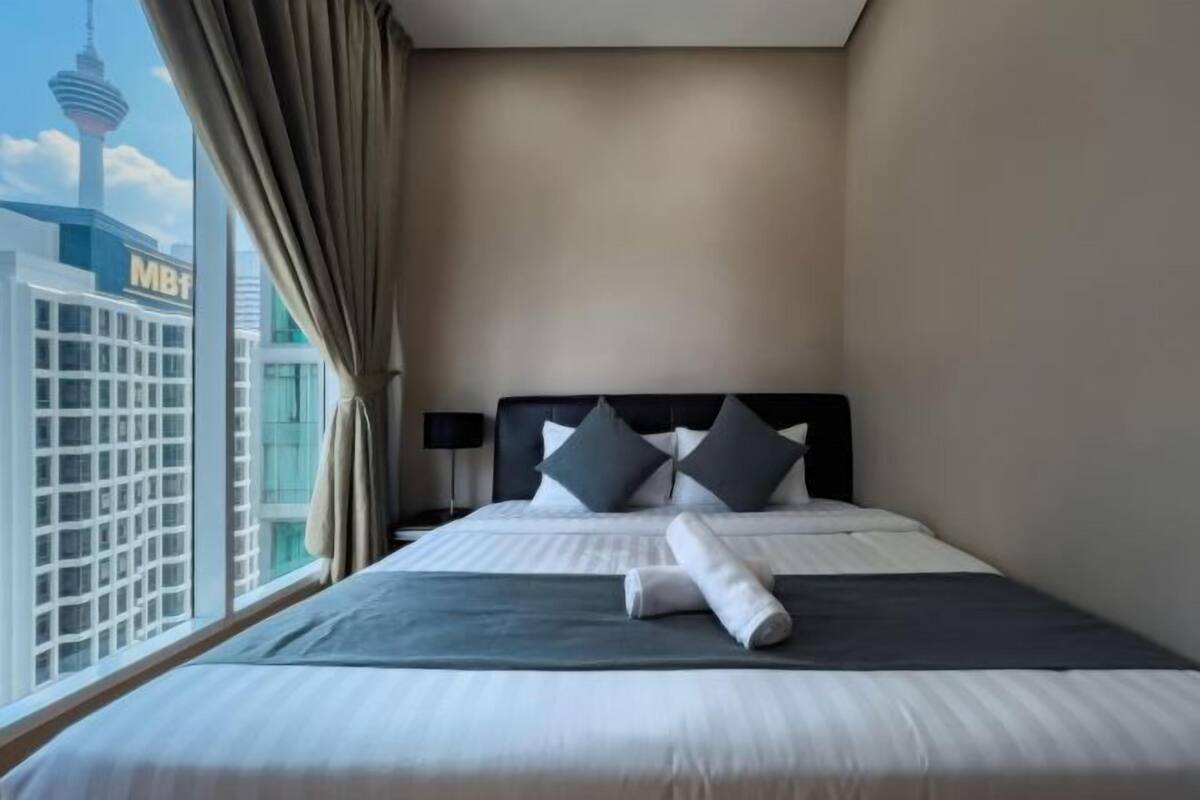 Une chambre d’hôtel avec un lit, des rideaux, une tête de lit et une vue sur le paysage urbain, qui comprend une tour.