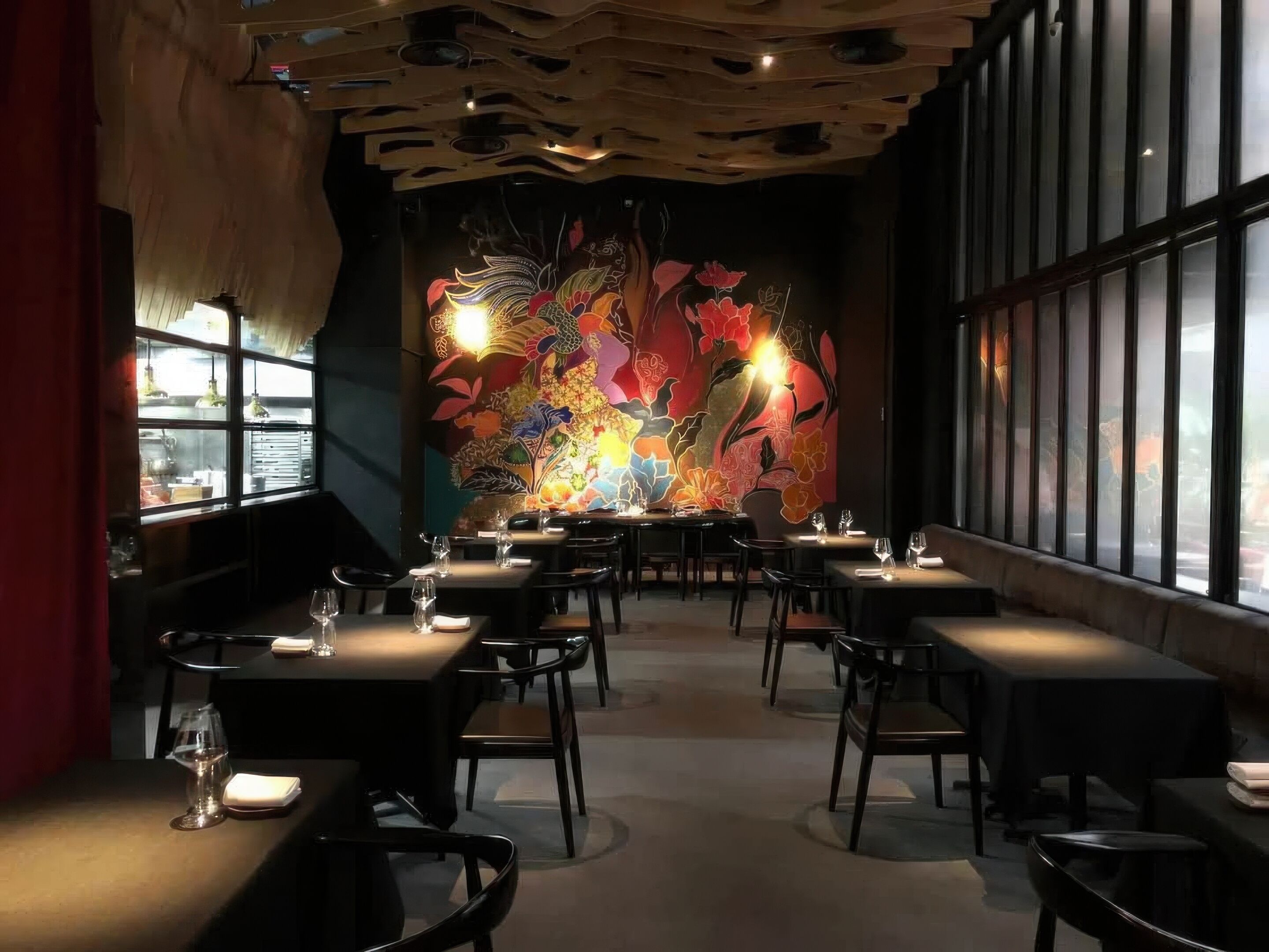 Un interior de restaurante con mesas y sillas, un mural grande en la pared y amplias ventanas.