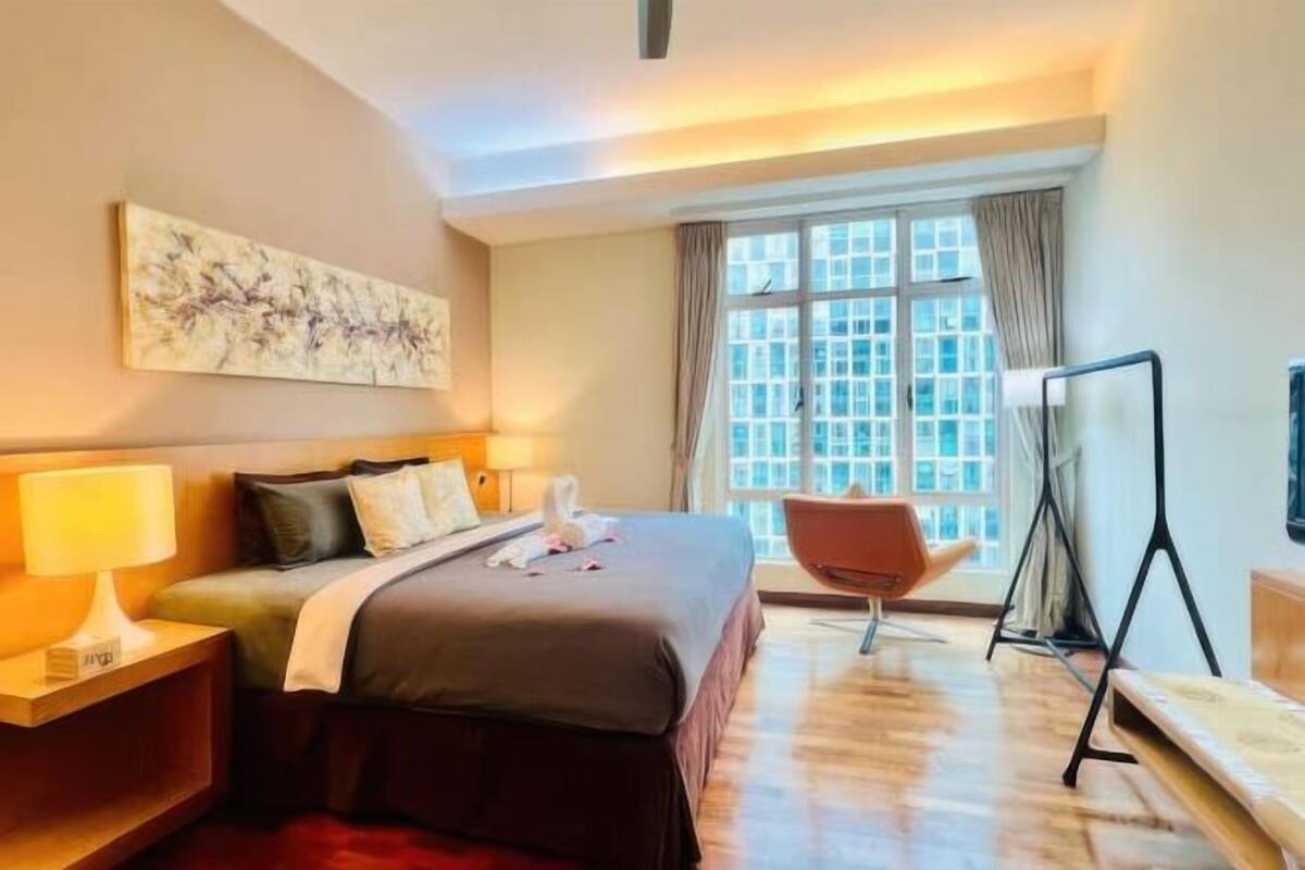 Une chambre d’hôtel avec un lit, des lampes de chevet, une chaise, une télévision et une grande fenêtre avec des rideaux.