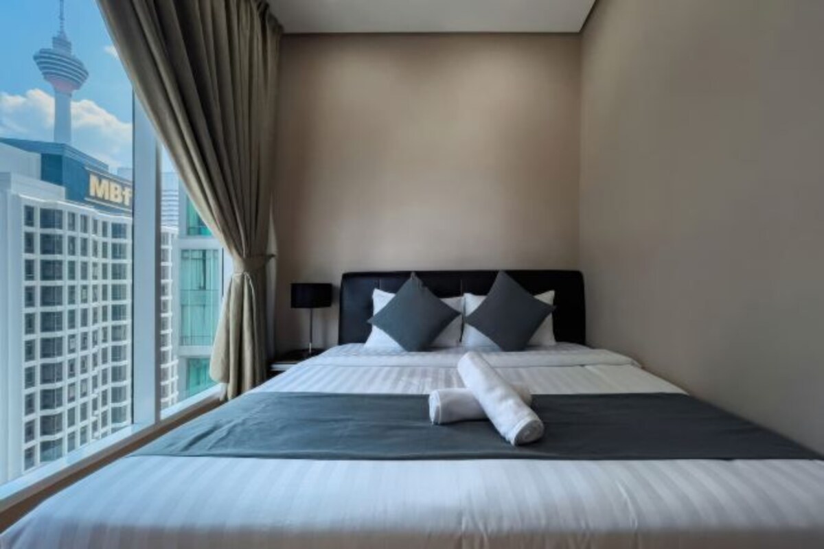 Une chambre d’hôtel avec un lit, des rideaux, une tête de lit et une vue sur le paysage urbain, qui comprend une tour.