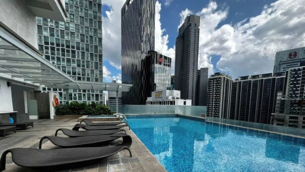 A rooftop pool with lounge chairs, surrounded by modern buildings and a clear sky.