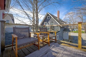 Eine Holzterrasse mit zwei Korbstühlen, einem Metallzaun und Blick auf ein Haus mit Schornstein.