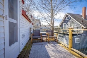 A covered outdoor deck with two wicker chairs and a small table, surrounded by a wooden fence and a metal railing.