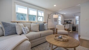 Un salon avec un canapé, des fauteuils, une table basse et une cuisine en arrière-plan.