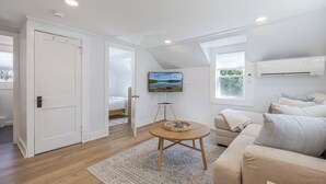 Une chambre moderne équipée d’un lit, d’une table ronde avec un plateau, d’un canapé, d’un téléviseur fixé au mur et d’un appareil de climatisation.