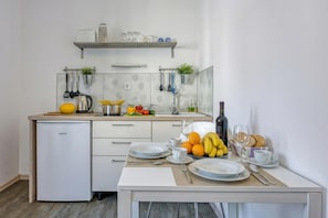 A compact kitchen with a refrigerator, a sink, and a dining area set with plates, cutlery, and a fruit bowl.