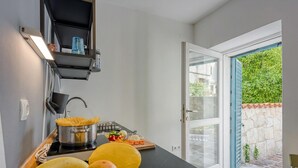 Una cocina con estufa, una olla, tabla de cortar con verduras y un frutero.