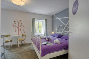 A bedroom with a bed, a desk, two chairs, a window, and a wall decoration.
